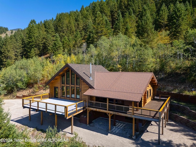 rear view of property featuring a wooden deck, log exterior, and a forest view