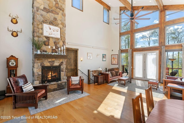 living room with a ceiling fan, wood finished floors, beamed ceiling, a fireplace, and a high ceiling