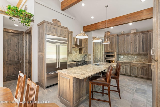 kitchen with an island with sink, beam ceiling, stainless steel appliances, backsplash, and light stone counters
