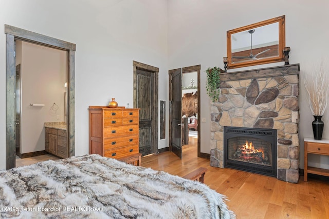 bedroom featuring baseboards, ensuite bathroom, a fireplace, and wood finished floors
