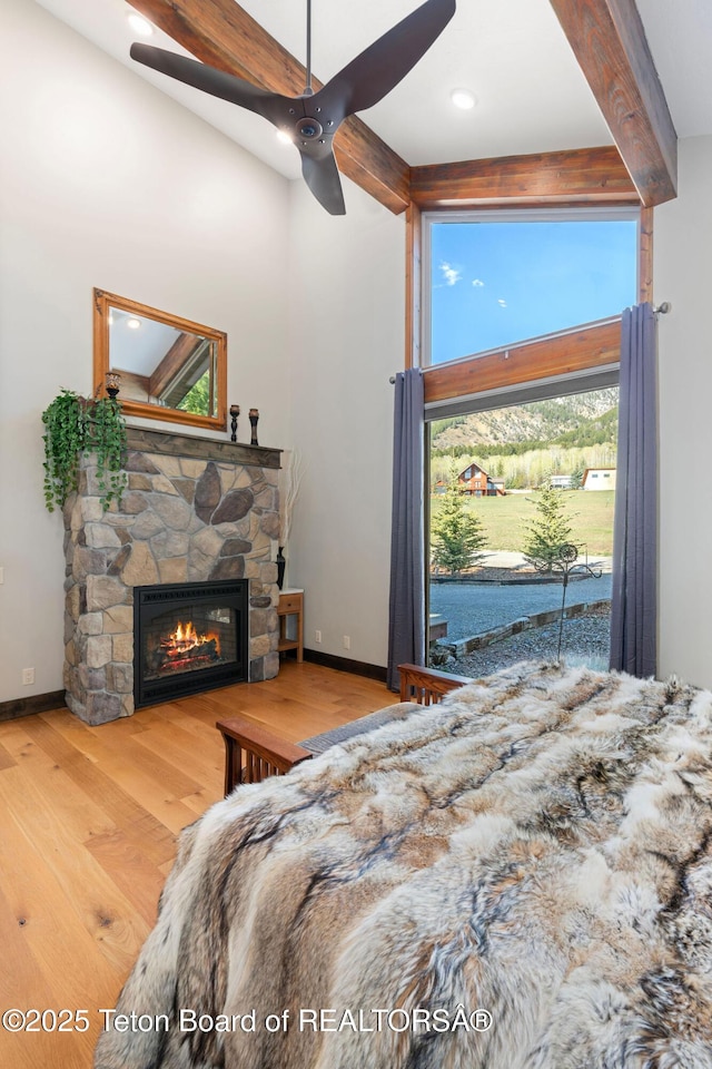 bedroom with beam ceiling, wood finished floors, ceiling fan, baseboards, and a stone fireplace