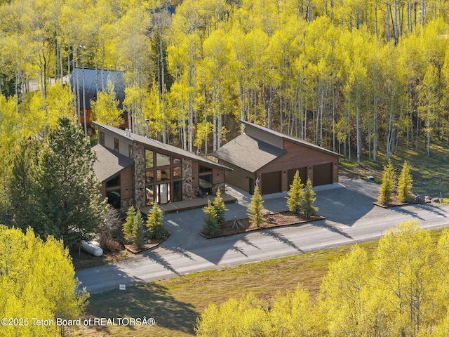 exterior space featuring concrete driveway, stone siding, and a wooded view