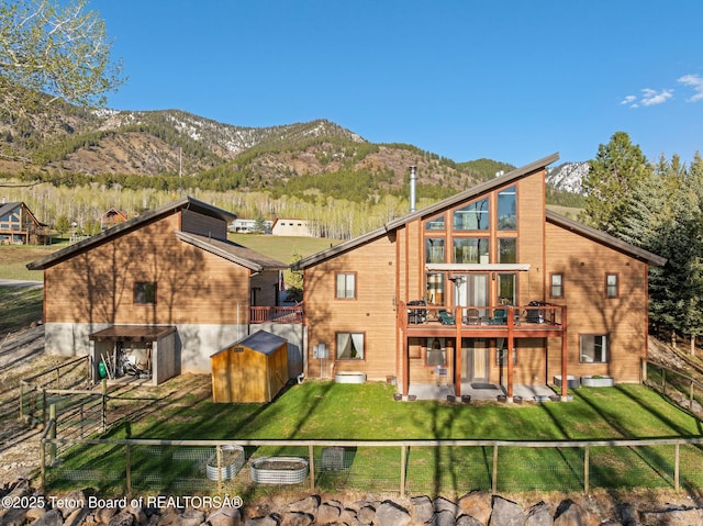 rear view of house with a lawn, a deck with mountain view, an outbuilding, and a fenced backyard