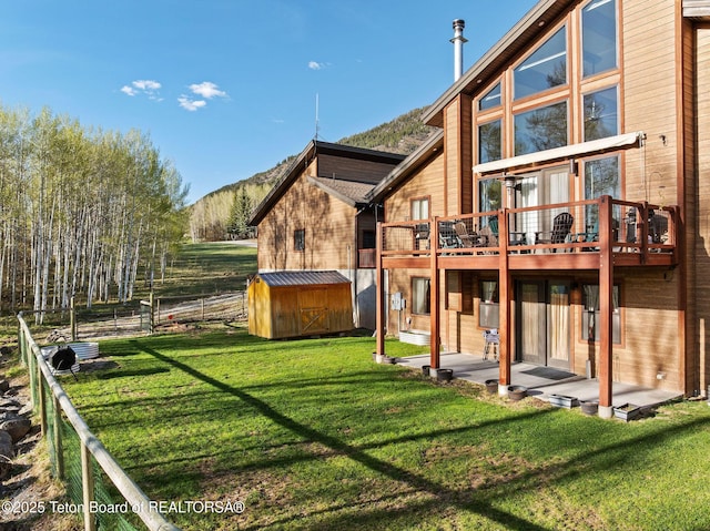back of property featuring an outdoor structure, a deck with mountain view, a lawn, and a storage unit