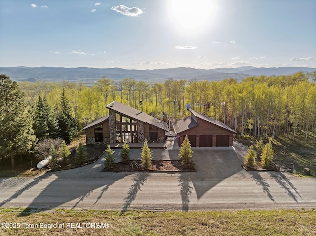 view of front of home with stone siding, a forest view, a mountain view, and driveway