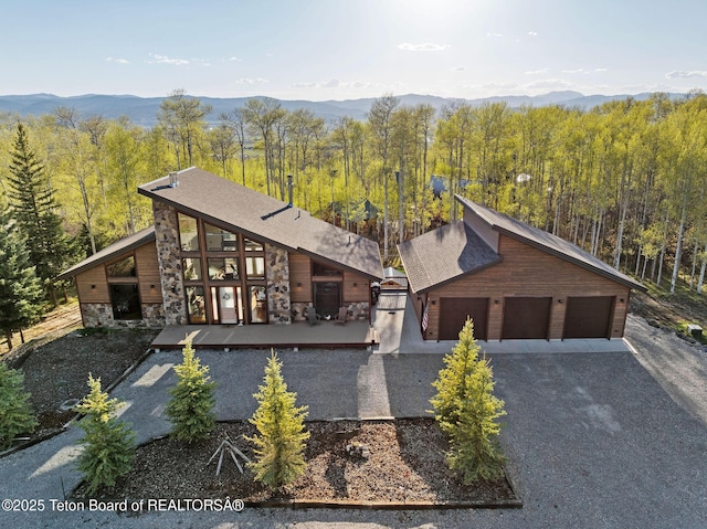 view of front of home featuring stone siding, a wooded view, and gravel driveway