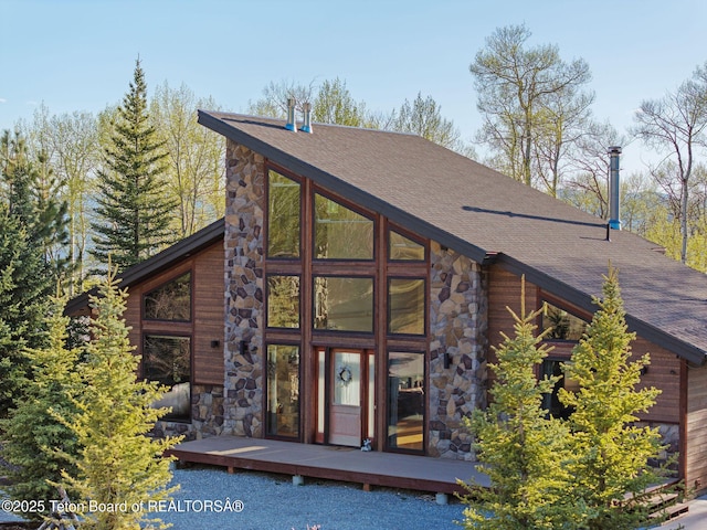 exterior space with stone siding, roof with shingles, and a deck