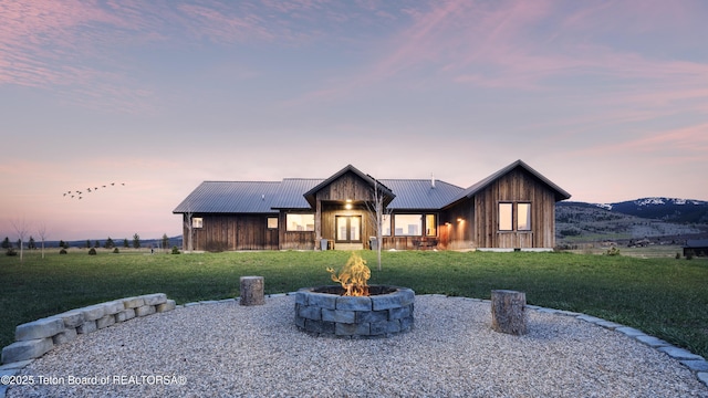 rustic home featuring a lawn, board and batten siding, an outdoor fire pit, and metal roof