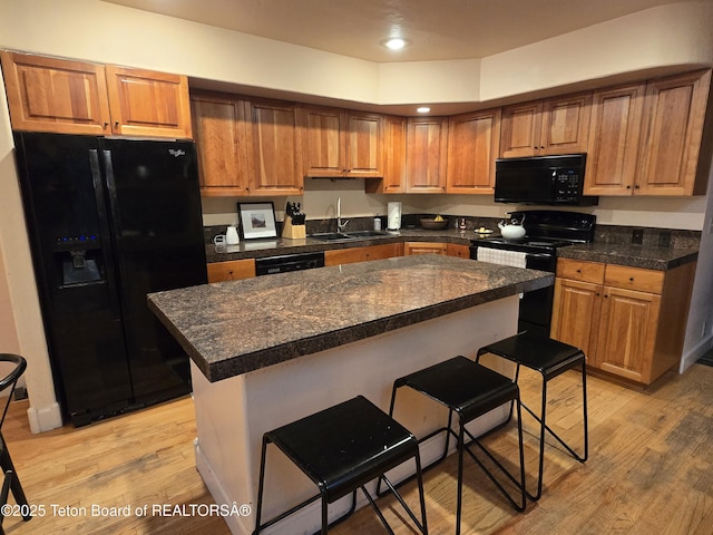 kitchen featuring a breakfast bar, a sink, black appliances, dark countertops, and light wood-type flooring