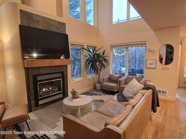 living room with wood finished floors, a towering ceiling, visible vents, a wealth of natural light, and a tile fireplace