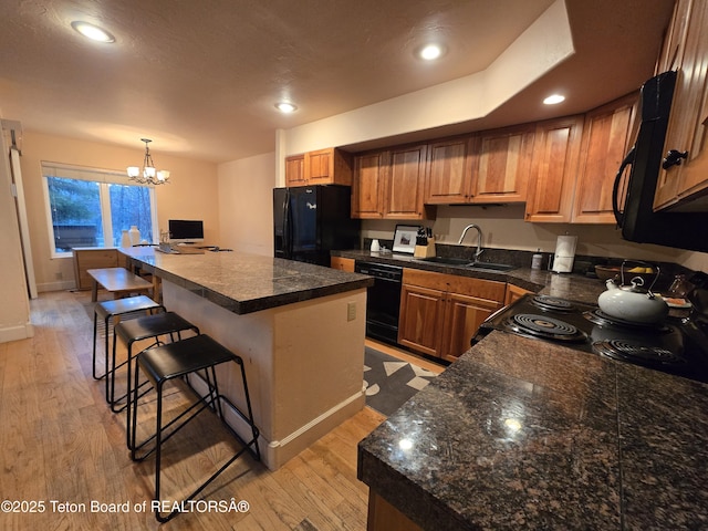 kitchen featuring a sink, a breakfast bar, tile countertops, black appliances, and a notable chandelier