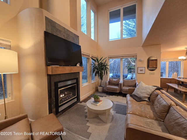 living area featuring a chandelier, a high ceiling, a tiled fireplace, and a wealth of natural light