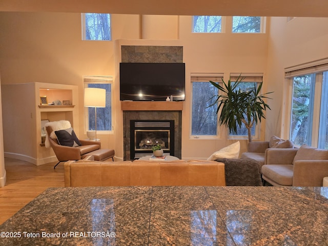 living area featuring baseboards, a glass covered fireplace, a towering ceiling, and wood finished floors