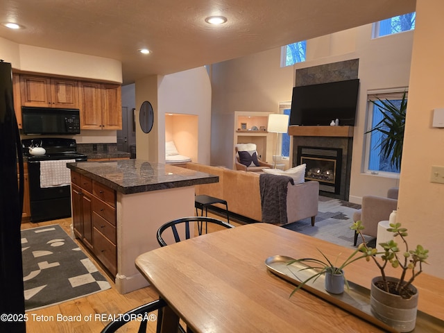 kitchen with a center island, a fireplace with flush hearth, black appliances, light wood-style floors, and recessed lighting