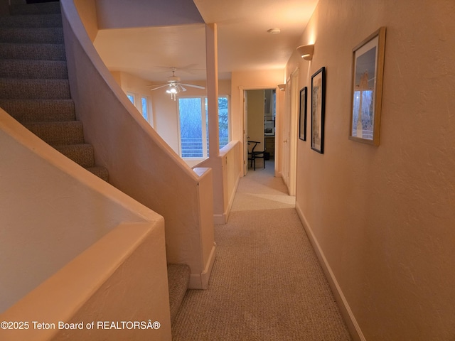 corridor featuring baseboards, stairway, and light colored carpet