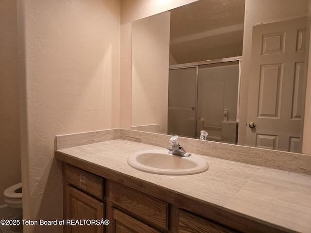 bathroom with a shower with door, toilet, a textured wall, and vanity