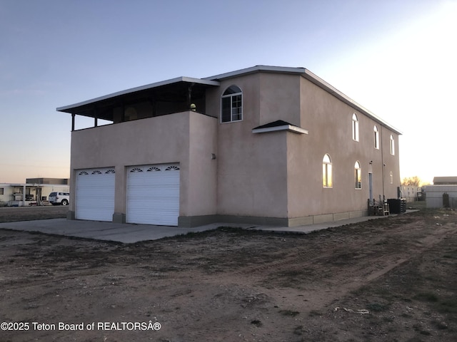 view of home's exterior with dirt driveway, stucco siding, a garage, and central AC