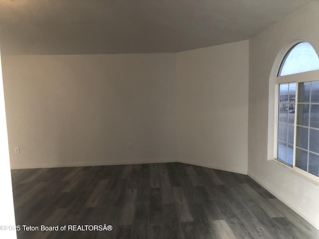 spare room with baseboards and dark wood-type flooring