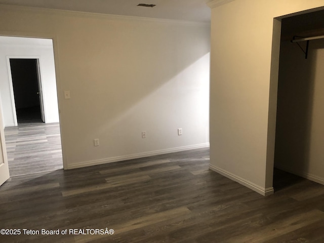 unfurnished bedroom with a closet, a walk in closet, baseboards, ornamental molding, and dark wood-style floors