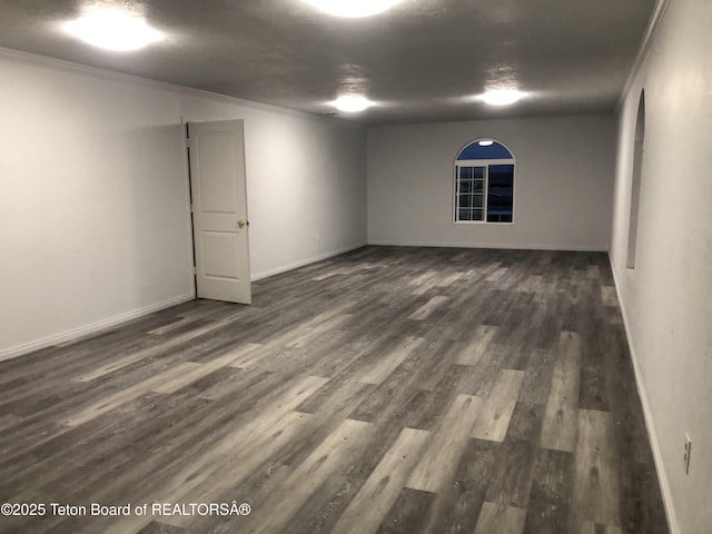 spare room featuring baseboards, ornamental molding, and dark wood-style floors