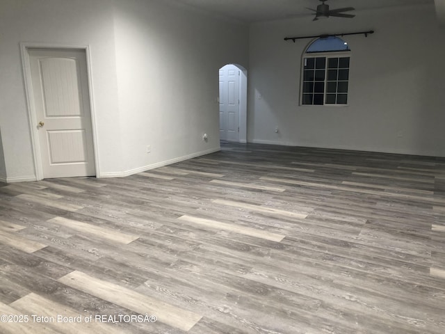 spare room with arched walkways, baseboards, a ceiling fan, and wood finished floors