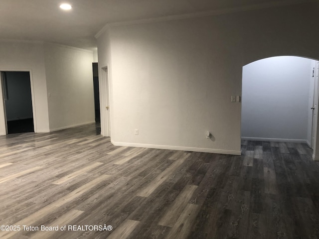 empty room with ornamental molding, dark wood finished floors, baseboards, and arched walkways