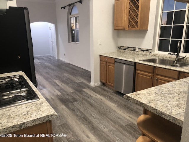 kitchen with a sink, stainless steel appliances, brown cabinets, arched walkways, and baseboards