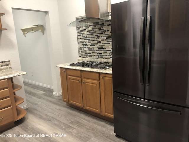kitchen featuring freestanding refrigerator, wall chimney exhaust hood, light wood-style floors, stainless steel gas stovetop, and tasteful backsplash