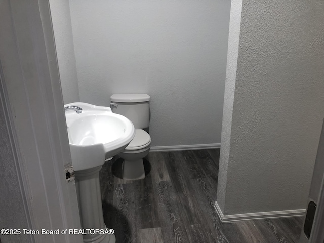 half bath with toilet, a textured wall, baseboards, and wood finished floors