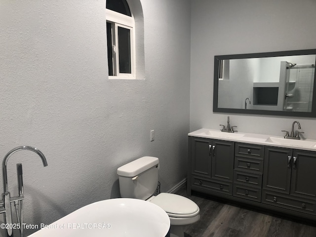 bathroom with a sink, double vanity, toilet, and wood finished floors