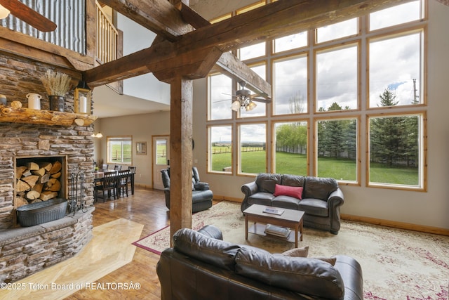 living area featuring baseboards, a stone fireplace, ceiling fan, wood finished floors, and a high ceiling