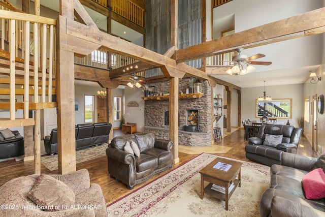 living room featuring a fireplace, a high ceiling, ceiling fan with notable chandelier, and wood finished floors