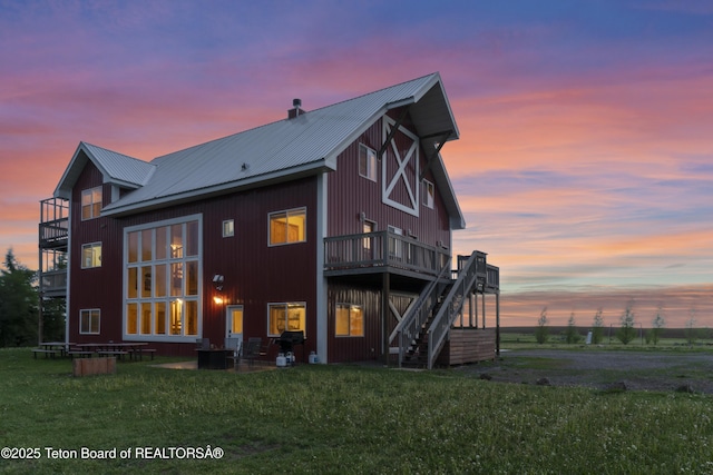 back of property featuring stairway, a wooden deck, metal roof, and a lawn