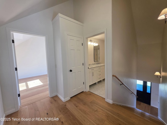 hallway featuring vaulted ceiling, baseboards, light wood-type flooring, and an upstairs landing