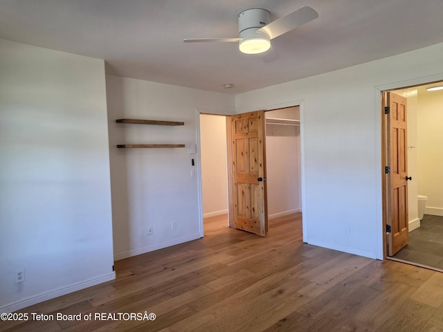 unfurnished bedroom featuring connected bathroom, wood finished floors, a closet, baseboards, and ceiling fan