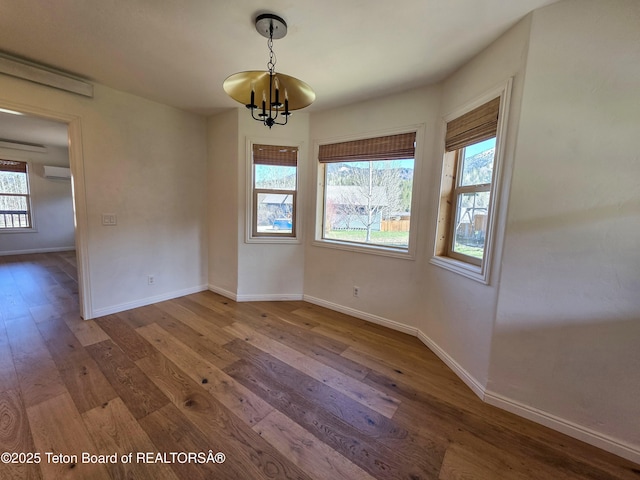 unfurnished dining area featuring an inviting chandelier, a wall unit AC, baseboards, and hardwood / wood-style floors