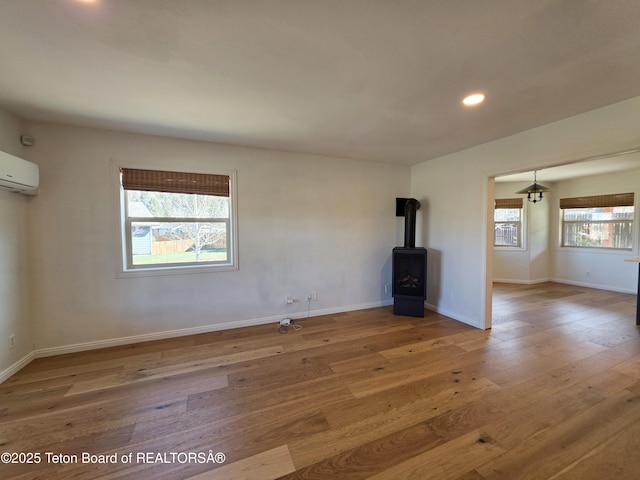 unfurnished living room featuring a wall mounted air conditioner, wood finished floors, a wood stove, recessed lighting, and baseboards