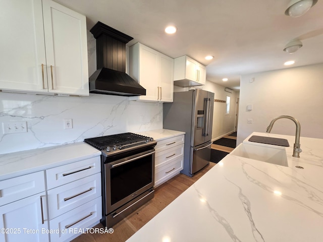 kitchen with wall chimney exhaust hood, stainless steel appliances, white cabinets, decorative backsplash, and light stone counters