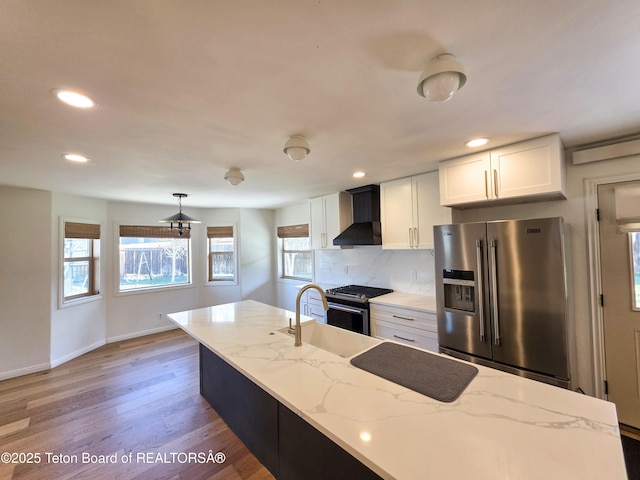 kitchen with a sink, stainless steel appliances, wall chimney range hood, recessed lighting, and white cabinets
