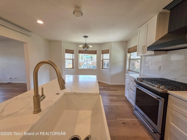 kitchen with a sink, wall chimney exhaust hood, backsplash, stainless steel gas range, and light wood-style floors