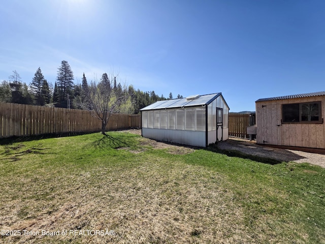 view of yard featuring a fenced backyard, a greenhouse, and an outbuilding