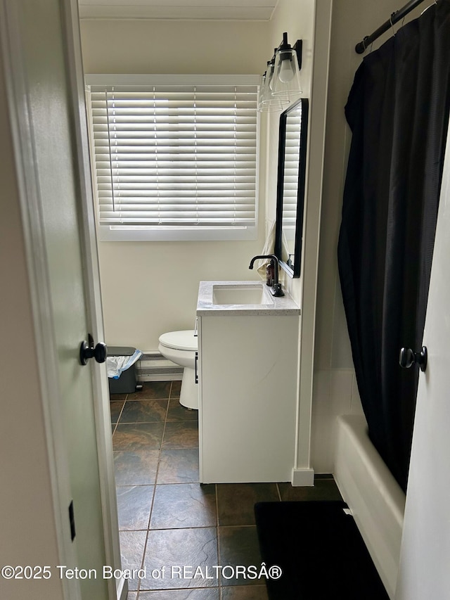 full bath with baseboards, vanity, toilet, stone tile floors, and shower / bathtub combination with curtain