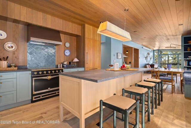 735 Snow King Dr, Jackson, WY 83001 - kitchen with wall chimney range hood, stainless steel electric range oven, dark countertops, light wood-style flooring, and wood ceiling