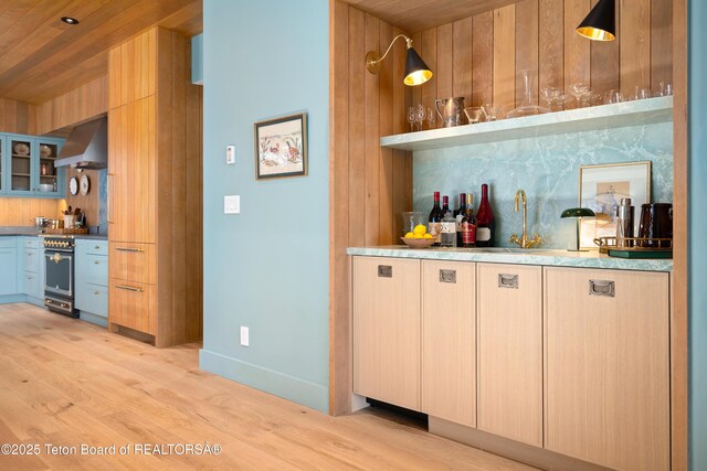 735 Snow King Dr, Jackson, WY 83001 - indoor dry bar featuring range hood, stainless steel gas range oven, light wood-style floors, baseboards, and wood walls