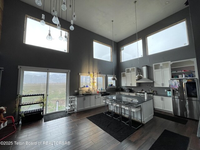 5860 Bitter Creek Rd, Afton, WY 83110 - kitchen featuring stainless steel fridge with ice dispenser, wall chimney range hood, dark countertops, a high ceiling, and white cabinets