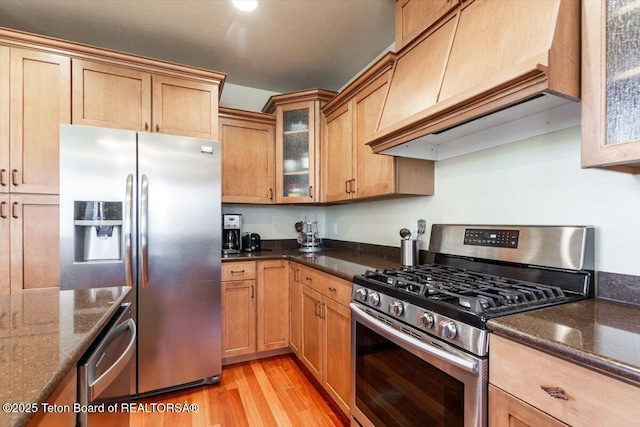 33 Willowbrook Dr, Driggs, ID 83422 - kitchen with appliances with stainless steel finishes, custom exhaust hood, light wood-style flooring, glass insert cabinets, and dark stone counters