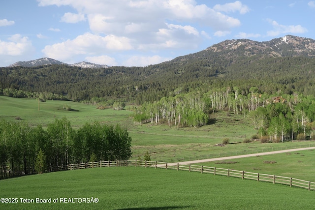 view of mountain backdrop featuring a forest and rural landscape