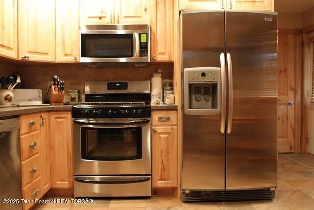 kitchen with stainless steel appliances, light tile patterned flooring, and dark countertops