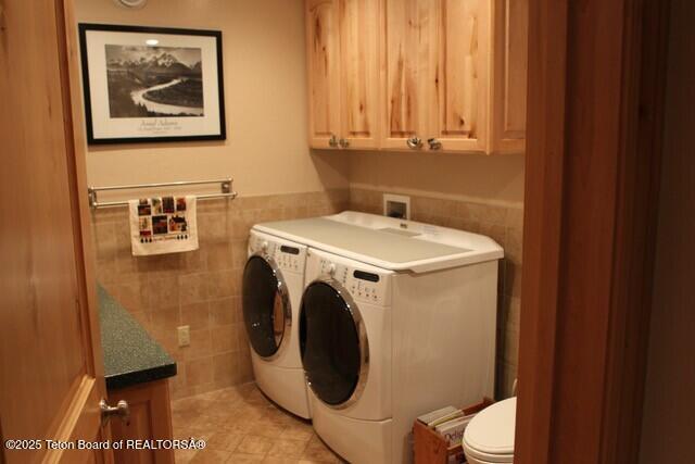 laundry area featuring tile walls, washer and clothes dryer, a wainscoted wall, and light tile patterned flooring