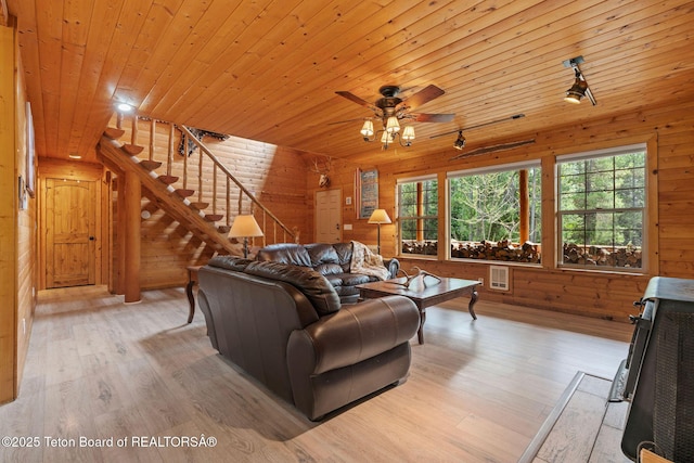 living area featuring light wood finished floors, wooden walls, a ceiling fan, stairs, and wood ceiling